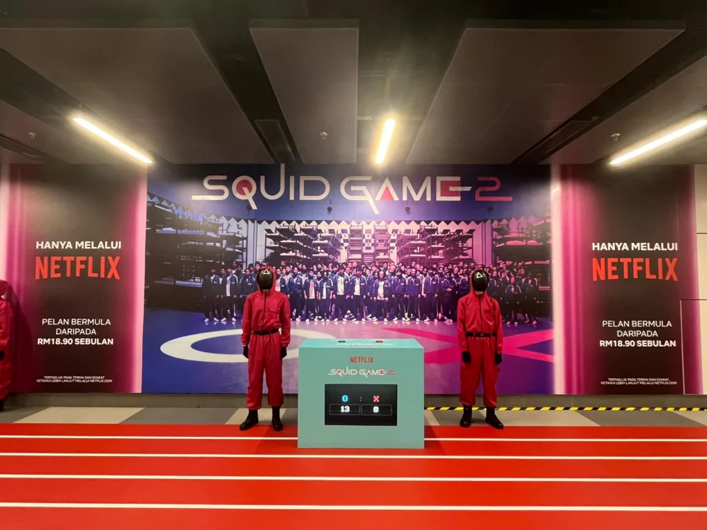 Squid Game 2 promotional installation with a voting console between two costumed guards at Ampang Park MRT Station.